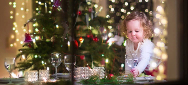 small girl playing with christmas decorations in front of red and purple decorated christmas tree